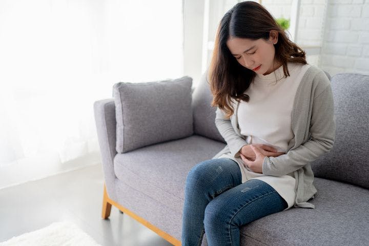 Women holds stomach in pain while sitting on couch.