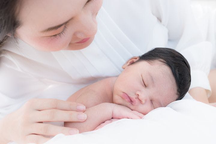 Asian mom dressed in white happily looking at her newborn baby