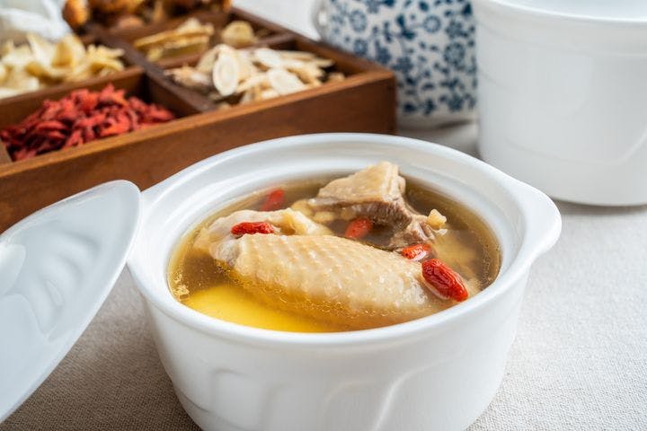 Chicken soup with goji berries in a bowl beside dried herbs in a wooden box