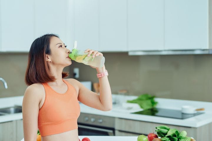 A woman drinking a bottle of lemon and cucumber infused water