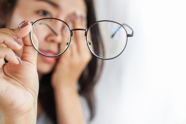 Woman looking at a pair glasses that she’s holding in her right hand while covering one eye with her left