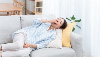 A woman lying sideways on the sofa while covering her yawn.