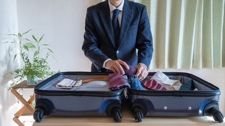 A businessman packing his suitcase with ties, shirts, and dress pants
