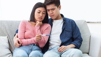 Young Asian couple sitting on a sofa with a pregnancy test in hand