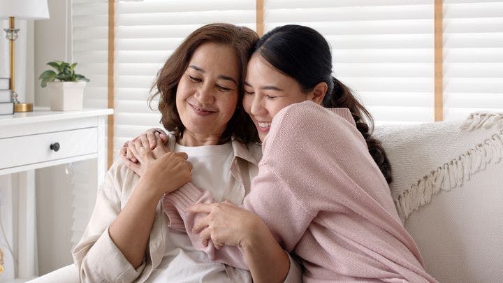 A middle-aged mother and her daughter embracing and smiling