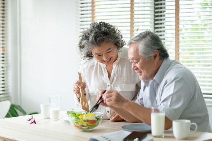 An elderly couple happily preparing a bowl of salad together