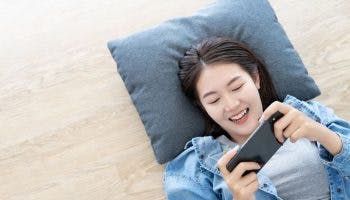A top view of a woman lying down on a pillow while playing with her mobile phone.