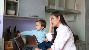 Woman working from home on laptop in the kitchen while also tending to her toddler.