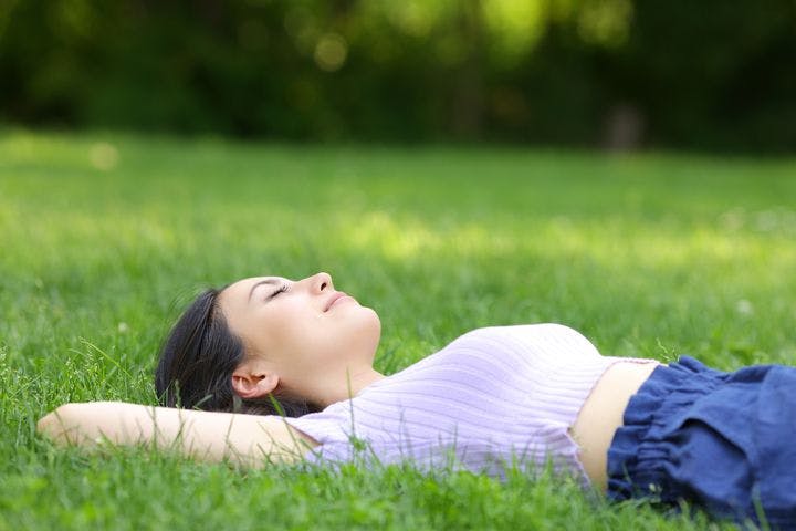 A side view of a woman lying on the grass with her eyes closed and a smile.
