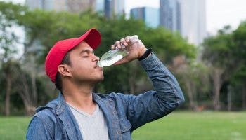 A young Asian man drinking a bottled water in a park