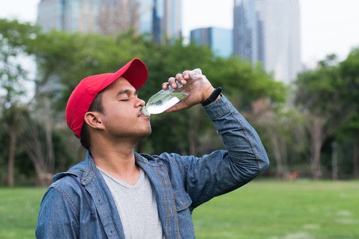 A young Asian man drinking a bottled water in a park