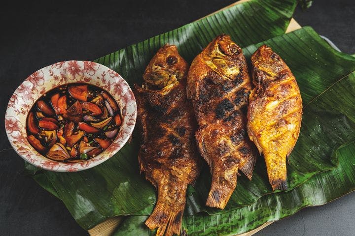 Ikan bakar served on a bed of banana leaves with a saucer containing soy sauce, and cut chillies and onions.