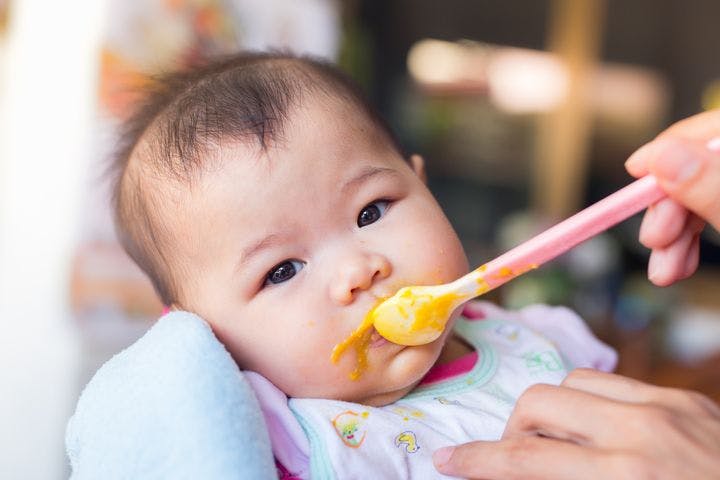 A baby being fed eggs; yolk smeared around their mouth.