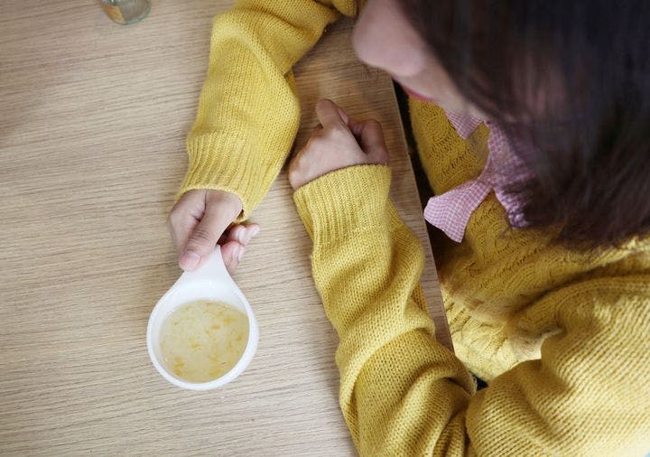 An aerial shot of a woman in a yellow sweater holding a cup of bird's nest soup