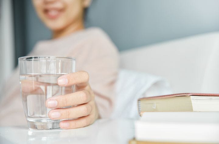 Woman smiling as she places a glass of water on a bedside shelf with her left hand