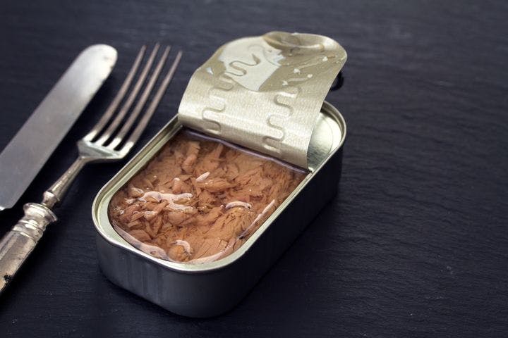 A half-opened can of tuna on a wooden background, with utensils next to it. 