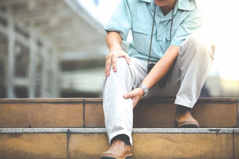 Man holding his right knee with both hands as he sits on the top step of a staircase