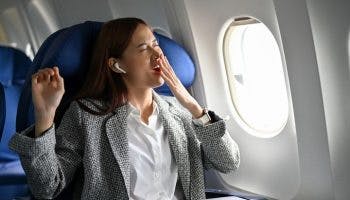 Woman yawning and tired due to jet lag, sitting on an airline seat