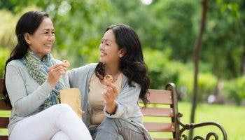 Two middle-aged women smiling at each other while holding cookies at an outdoor park