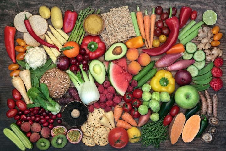 Various colourful fruits, vegetables, roots, and grain foods against wooden background