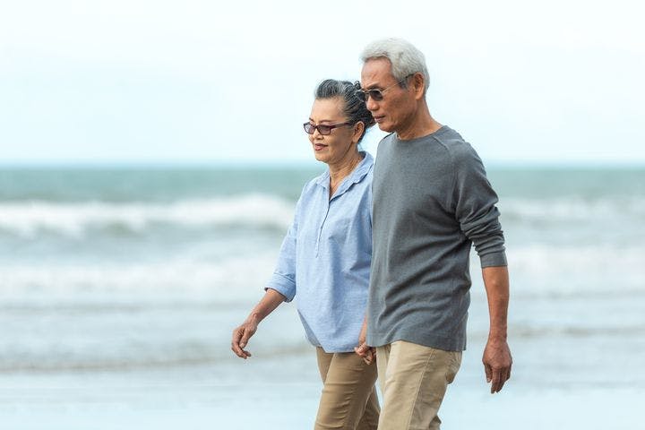 An older couple walking hand in hand on a beach.