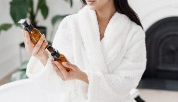 A partial view of a woman in bathrobe holding two skincare products in her hands.