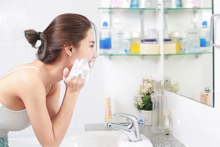 A woman cleansing her face in front of a bathroom mirror