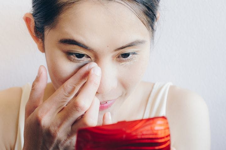 Woman applying concealer under her eyes to mask dark eye bags
