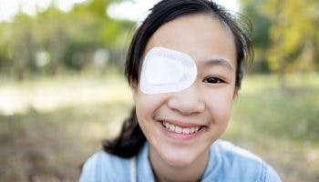 Young girl smiling with a white eye patch on.