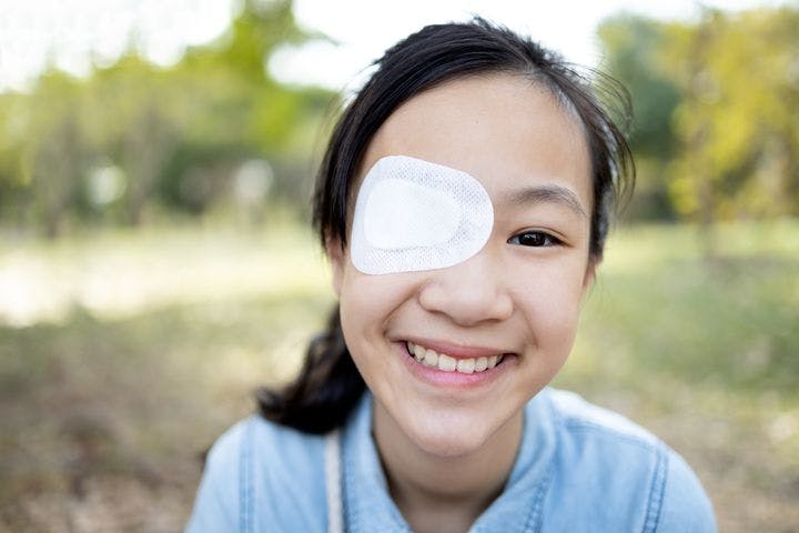 Young girl smiling with a white eye patch on.