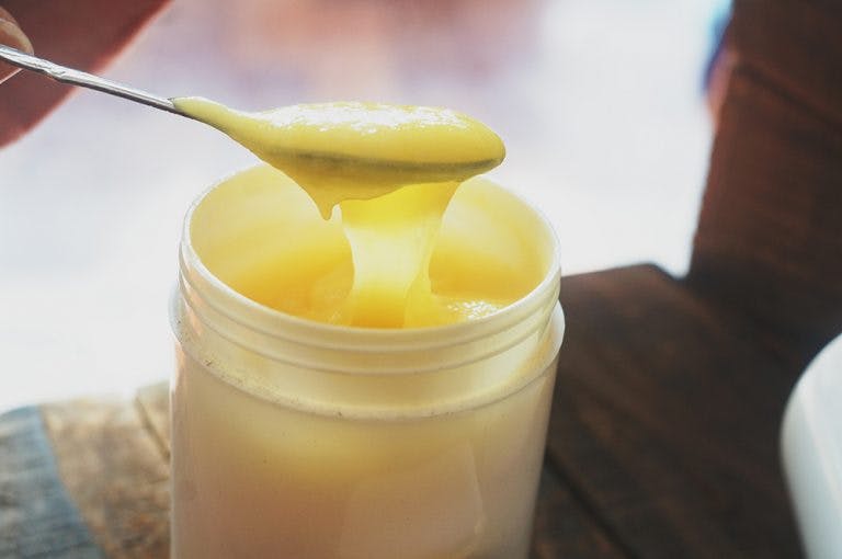 A closeup image of a spoon dipping into a jar of royal jelly product