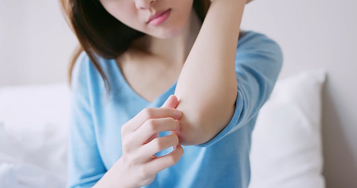 A woman scratching a dry patch of skin on her elbow using her fingertips