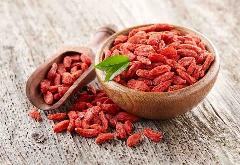 A bowl of red goji berries on a wooden surface