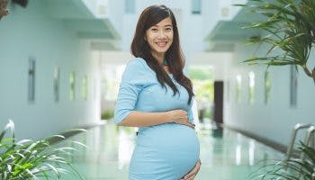 A young pregnant woman in a light blue dress holding her belly