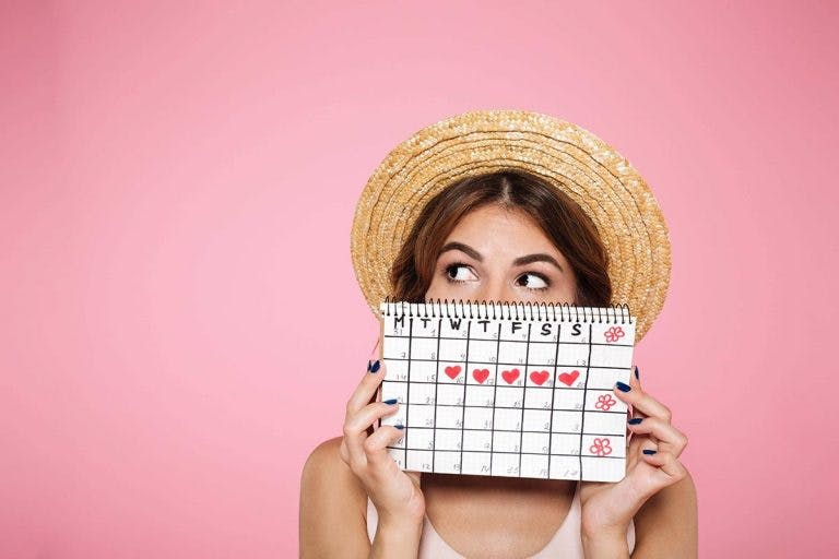 Woman wearing a straw hat holding a self-drawn calendar in front of her face