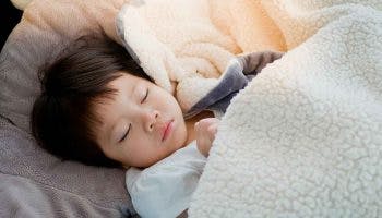 Child sleeping in his bed under a wool blanket