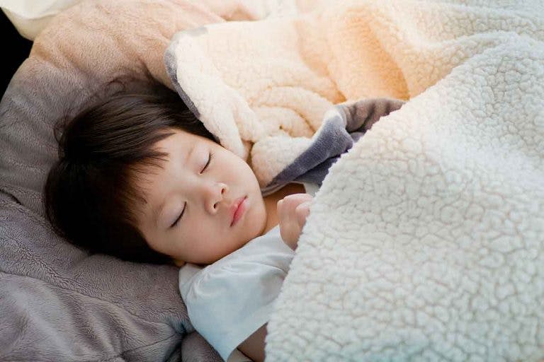 Child sleeping in his bed under a wool blanket