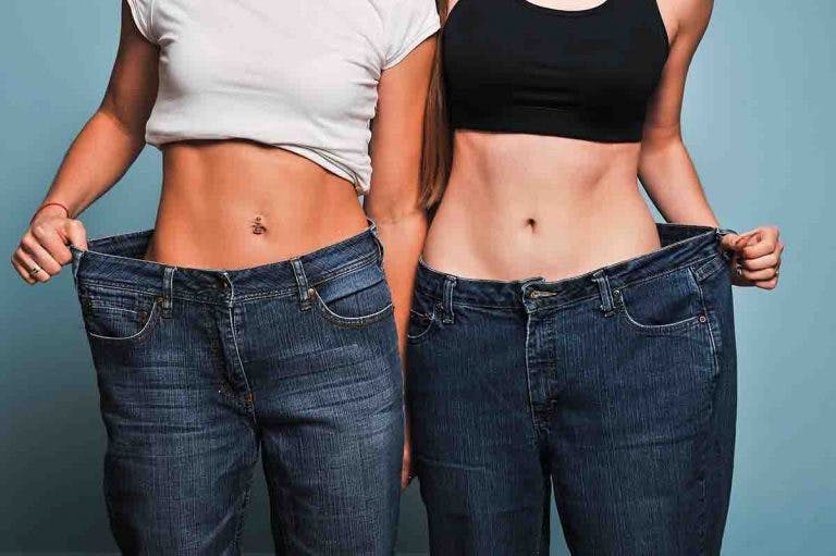 Two women stand next to each other and pull the waistband of their oversized jeans