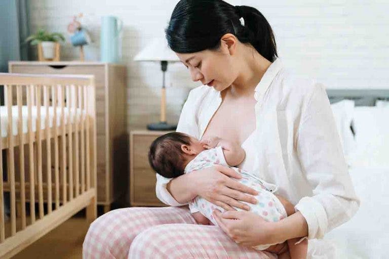 Asian mother breastfeeding her newborn in the bedroom while sitting on the bed