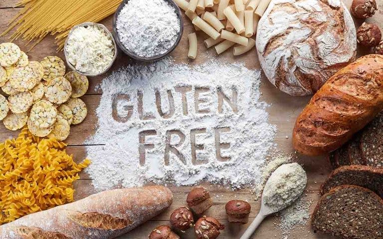 Top view of gluten-free food, including pasta, bread, snacks, and flour on wooden background