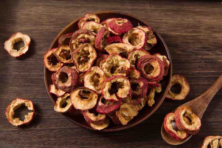 Dried hawthorn berry slices in a bowl on a wooden background