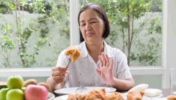 Senior Asian woman holds a fried chicken but shows her lack of appetite