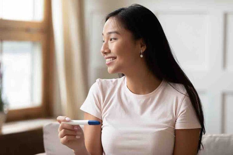 A young Asian woman smiles while holding pregnancy test result