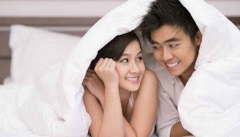 Young Asian couple looking at each other and smiling under a blanket
