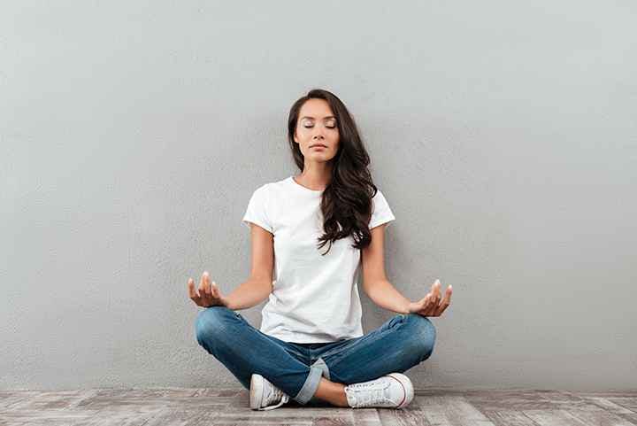Woman in casual wear sitting with eyes closed and legs crossed while meditating