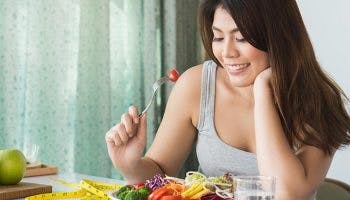 Woman having a bowl of salad with a measurement tape next to her 