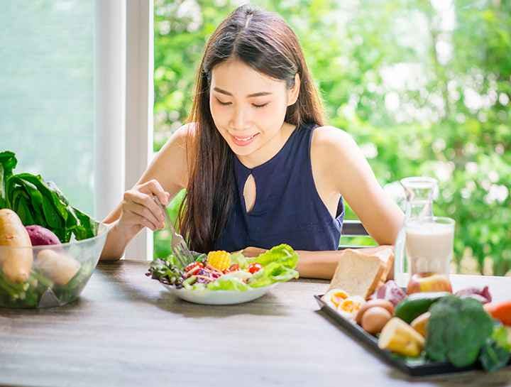 A young woman eating a plate of fresh salad with a variety of healthy foods next to her 