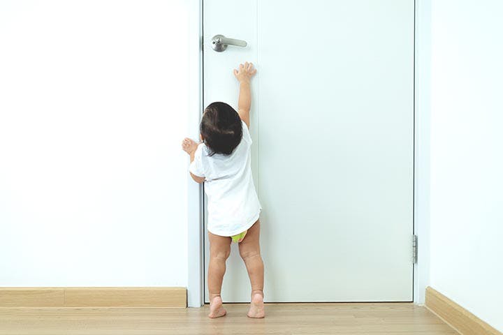 Toddler standing on tiptoes reaching for a doorknob.