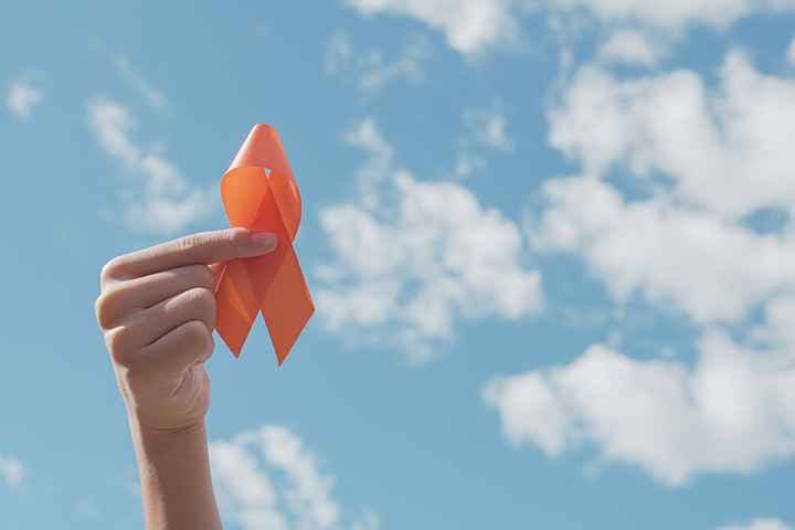 Hand holding yellow ribbon against blue sky for multiple sclerosis awareness