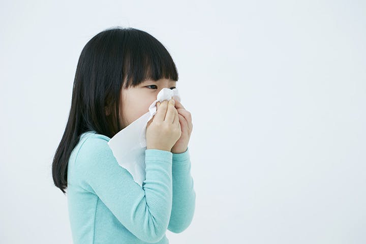 Sick girl sneezing into a tissue